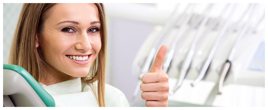 Smiling woman at dentist, thumbs up.