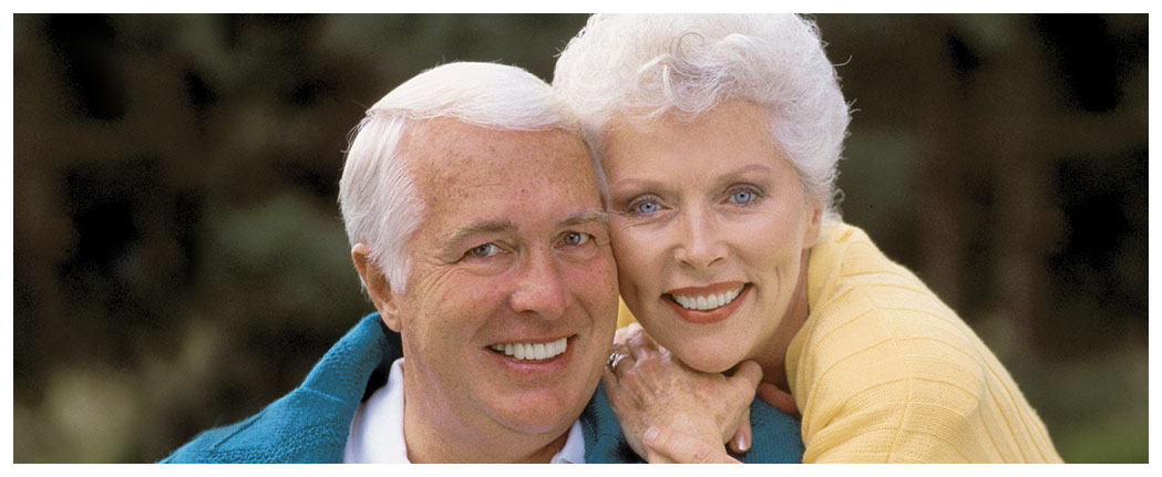 Smiling elderly couple posing together outdoors.