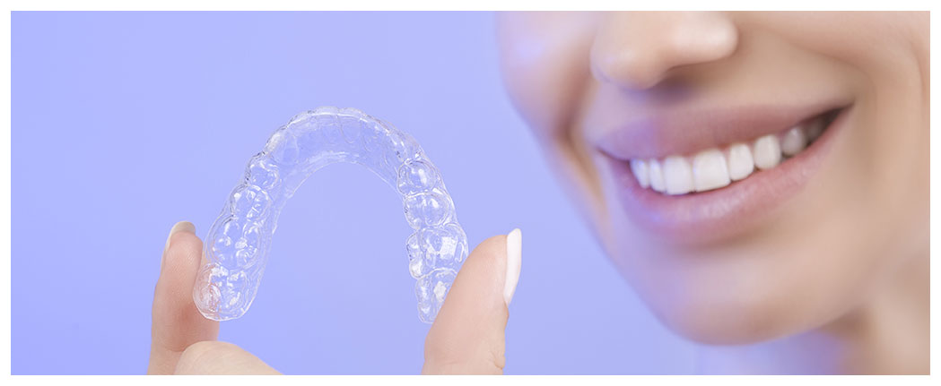 Woman holding clear dental aligner, smiling.