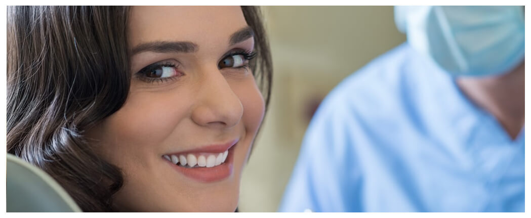 Smiling woman beside masked dentist.